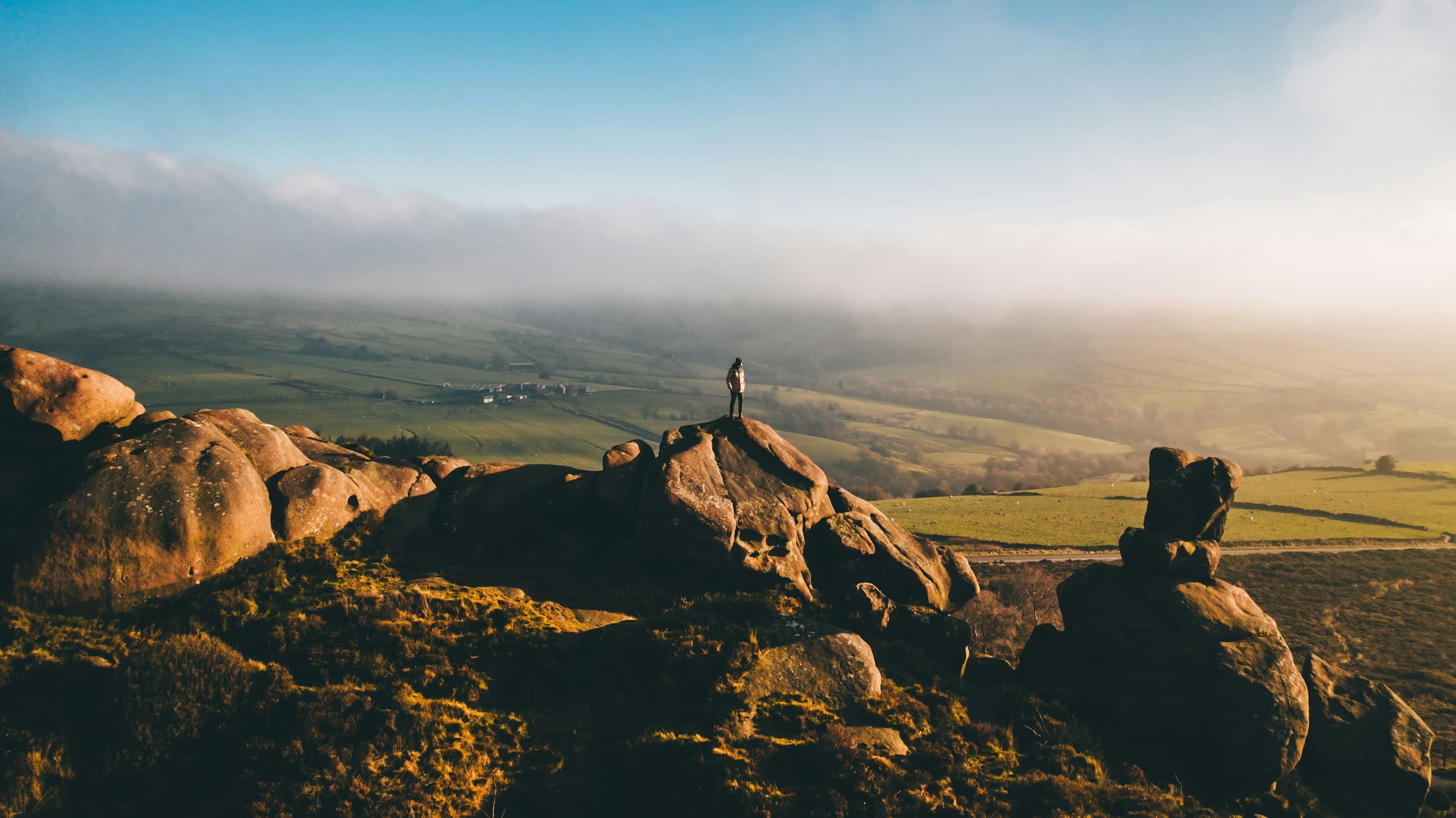 A walker on a gritstone outcrop above open country